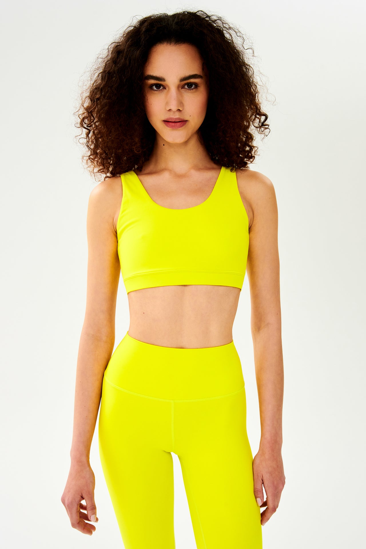 Front view of woman with curly dark wearing bright yellow bra with bright yellow leggings