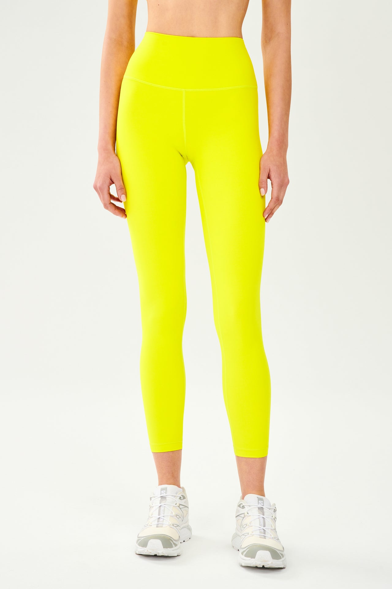 Front view of model wearing bright yellow high waist  leggings and white shoes