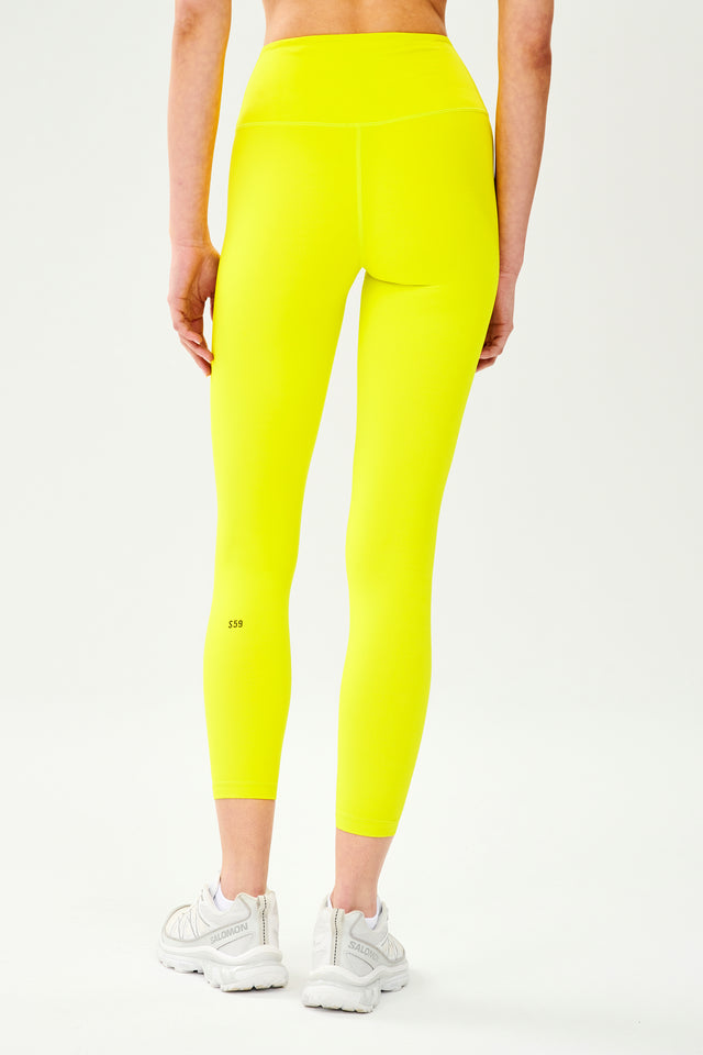 Back view of model wearing bright yellow high waist leggings and white shoes