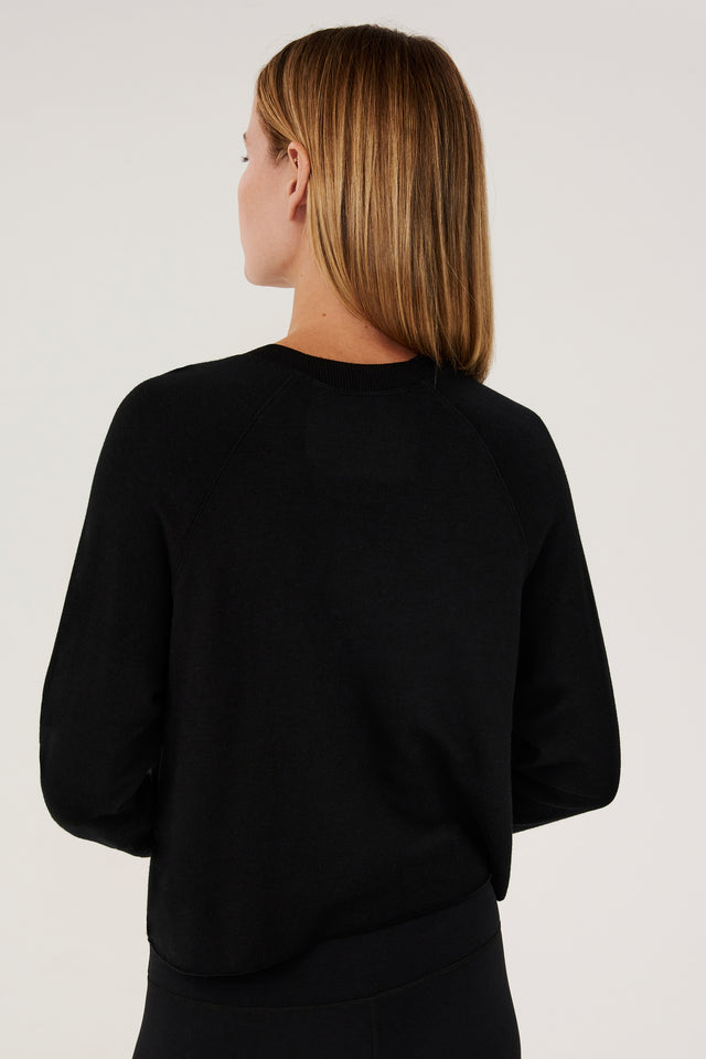 Back view of woman with dark blonde hair, wearing black cropped sweatshirt with black leggings