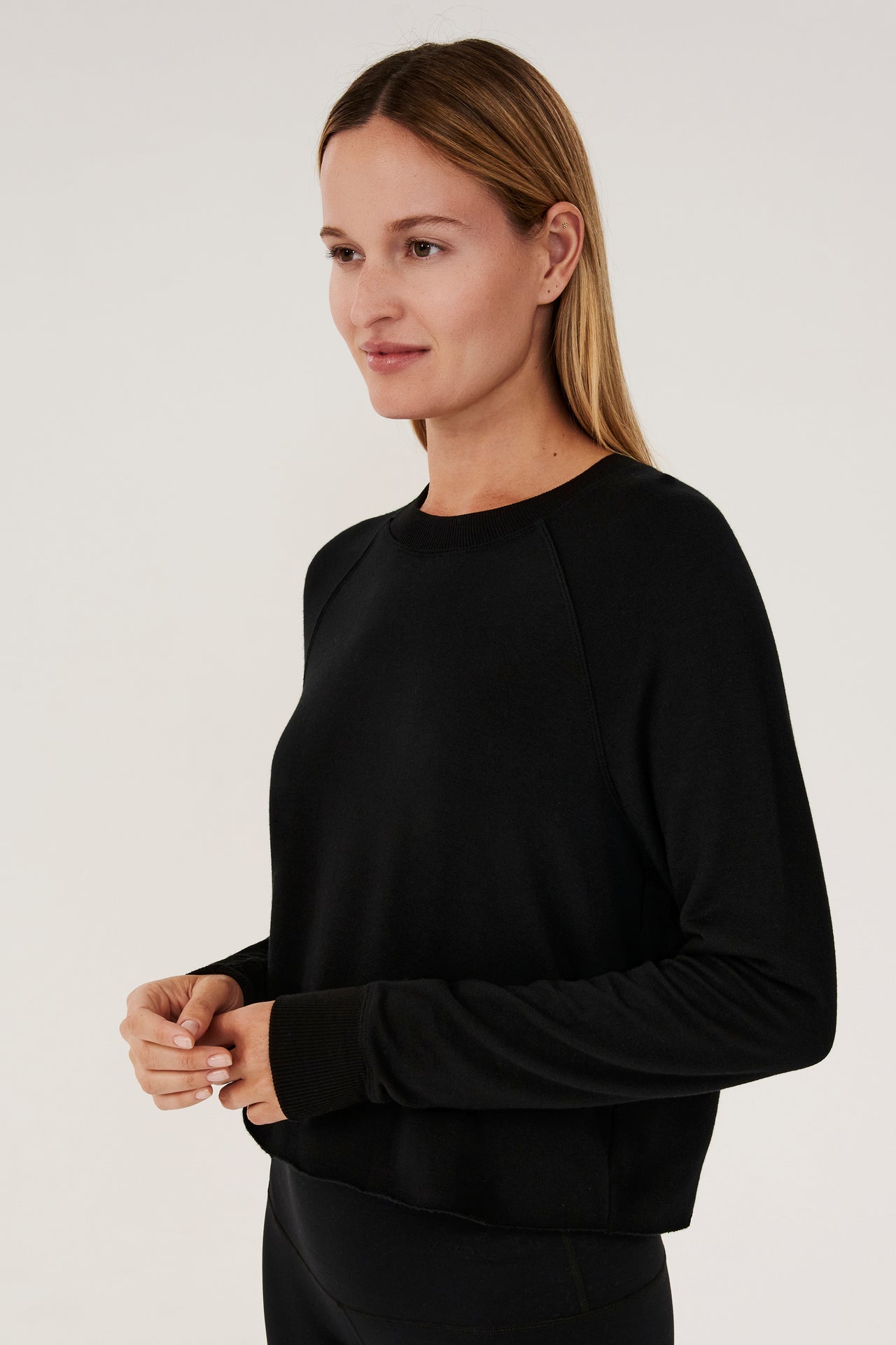Front side view of woman with dark blonde hair, wearing black cropped sweatshirt with black leggings