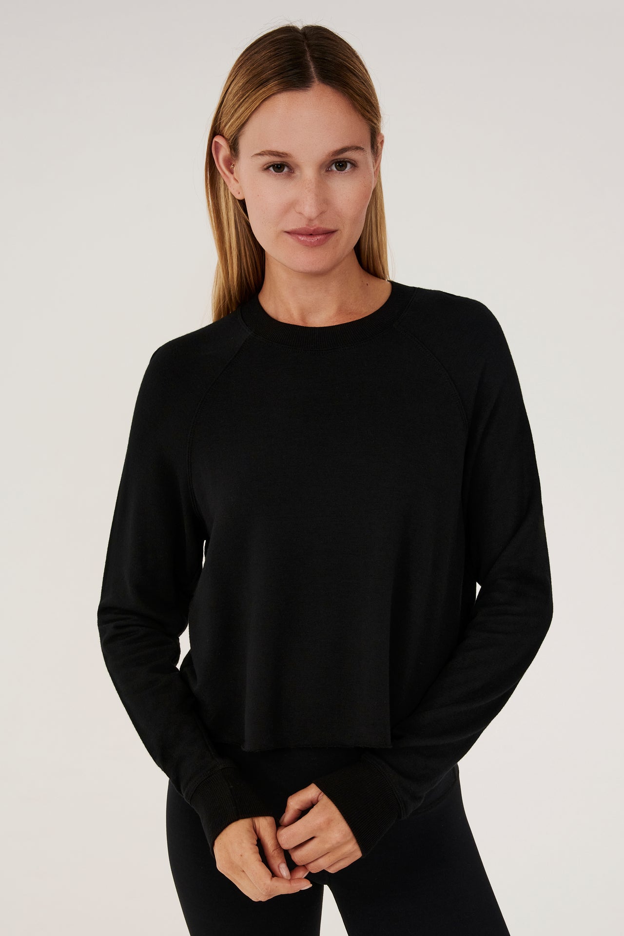 Front view of woman with dark blonde hair, wearing black cropped sweatshirt with black leggings