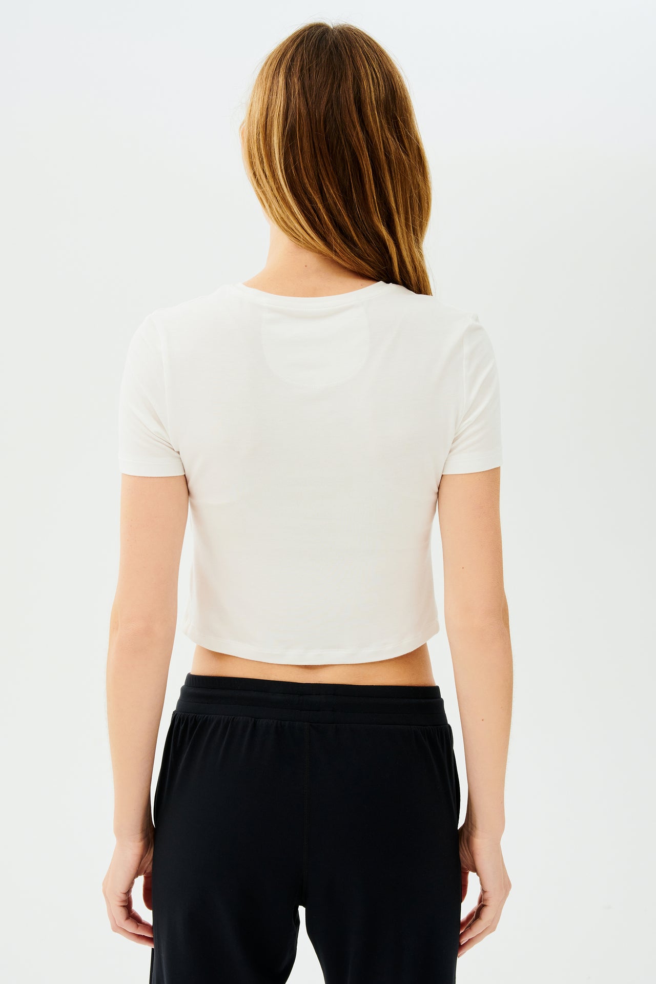 The back view of a woman wearing a SPLITS59 Daisy Jersey Tee in White and black high waist leggings.