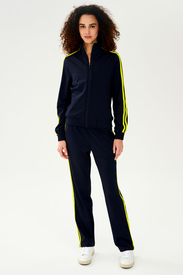 A woman warming up in a SPLITS59 Fox Techflex Jacket - Indigo/Chartreuse, navy with yellow side stripes.