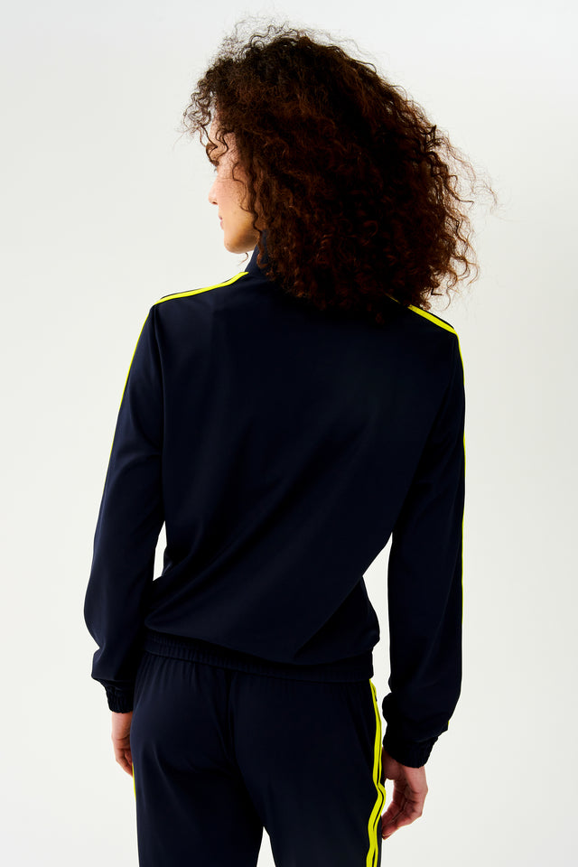 The back view of a woman in a luxurious SPLITS59 Fox Techflex Jacket in Indigo/Chartreuse, ideal as an après workout piece.