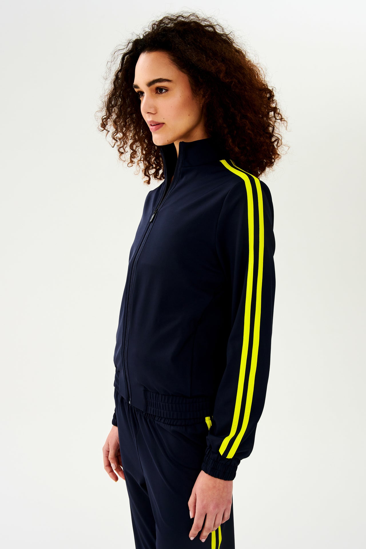 A woman wearing a luxurious SPLITS59 Fox Techflex Jacket in Indigo/Chartreuse with warming up.