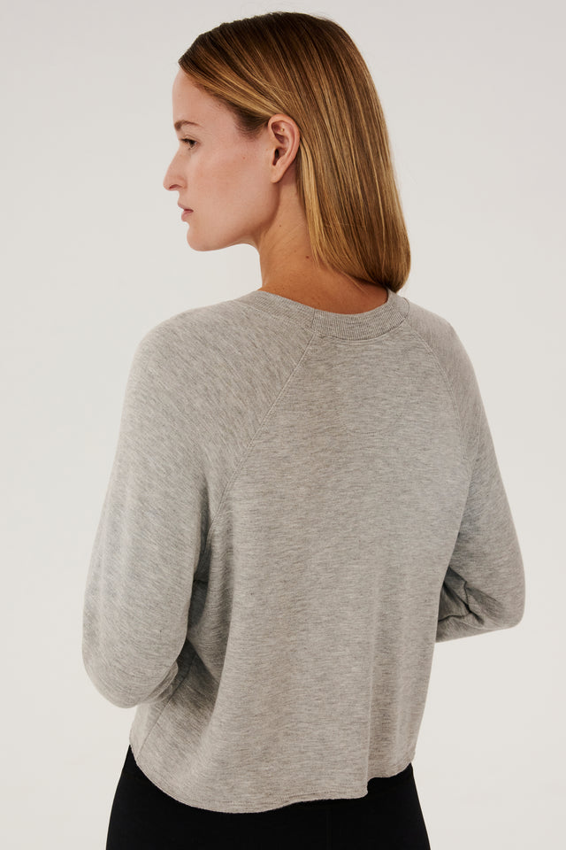 Back side view of woman with dark blonde hair, wearing grey cropped sweatshirt with black leggings