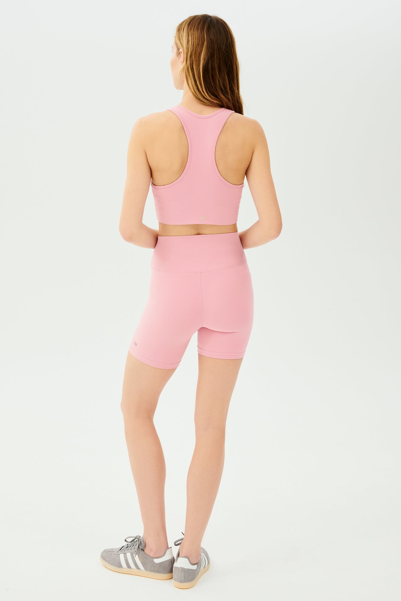 Full back view of girl wearing highwaisted mid thigh pink bike shorts with pink sports bra and grey shoes