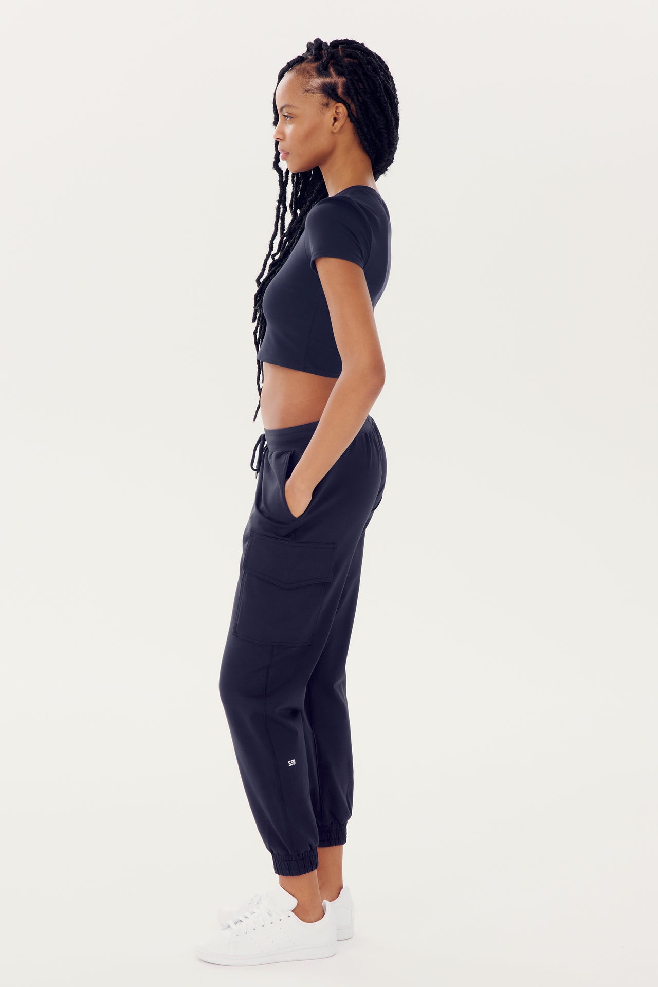 A woman wearing a SPLITS59 Airweight S/S Crop - Indigo and sportswear, standing in profile against a white background.