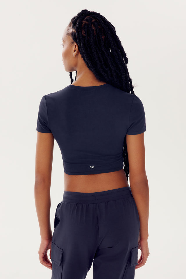Woman wearing a navy blue SPLITS59 Airweight S/S Crop top and matching workout pants from the back view.
