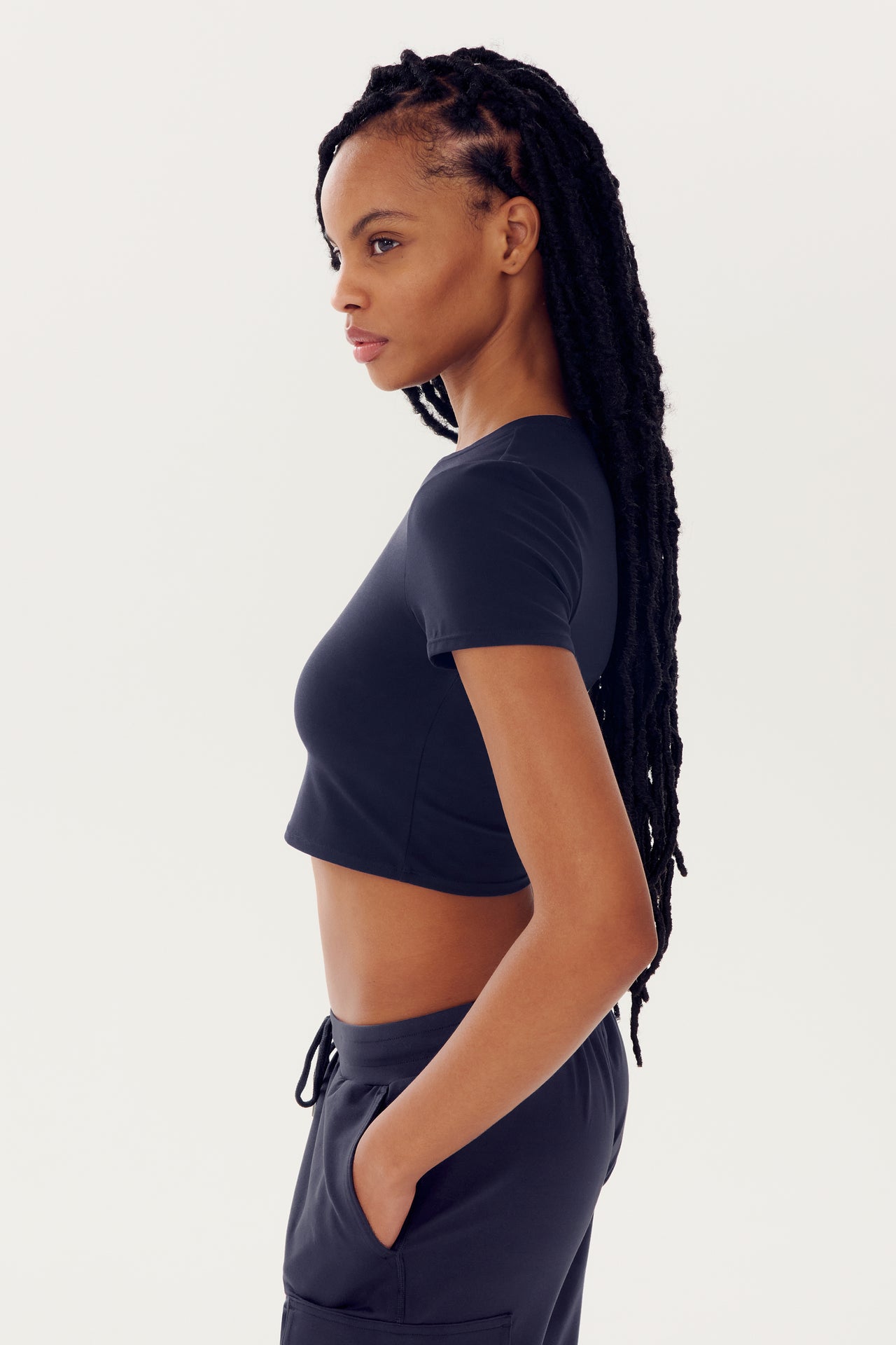 Side profile of a woman with braided hair wearing an SPLITS59 Airweight S/S Crop - Indigo top and high-waisted pants.