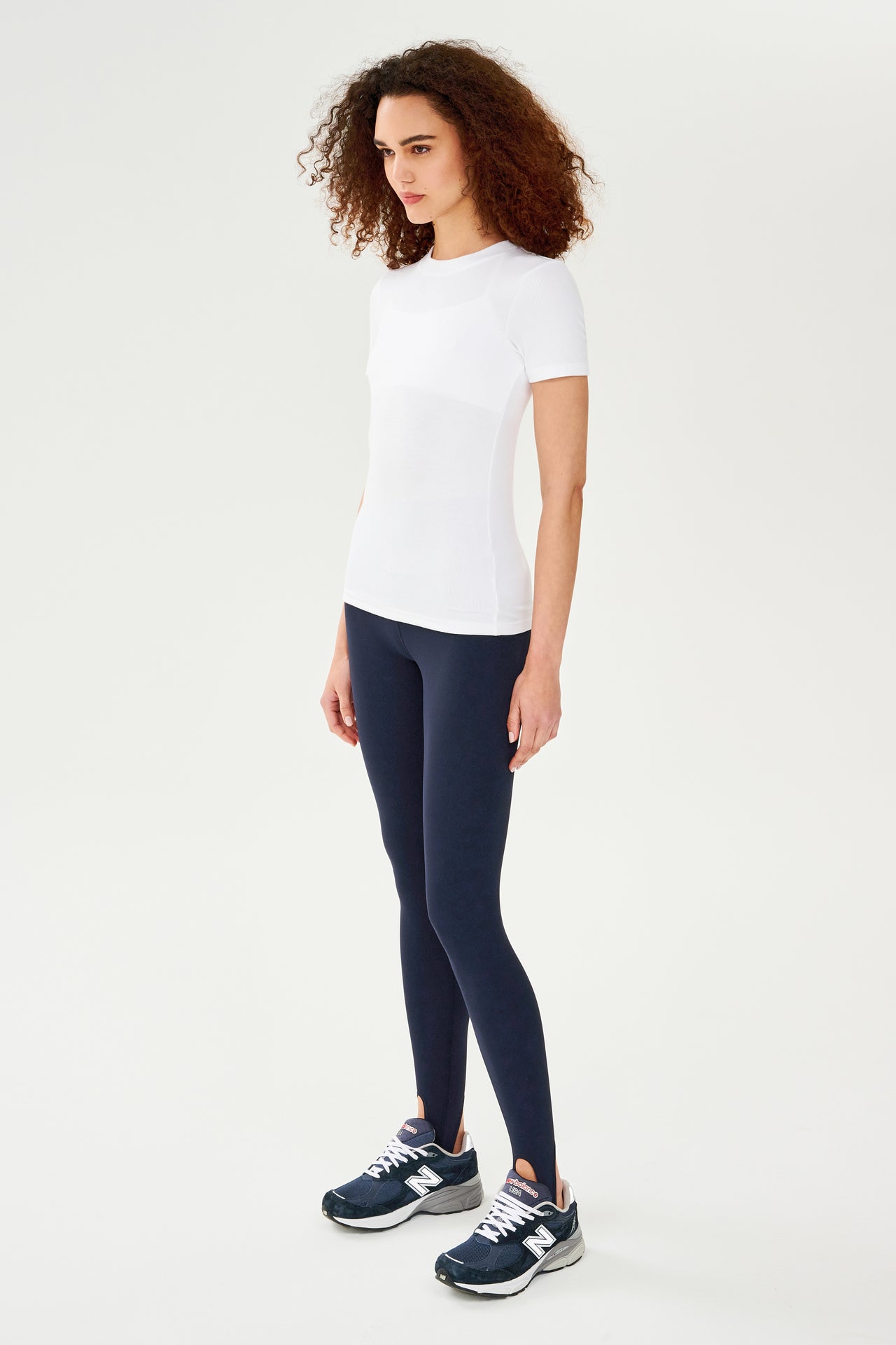 A woman wearing a SPLITS59 Louise Rib Short Sleeve - White t-shirt and black leggings, ready for her yoga session.