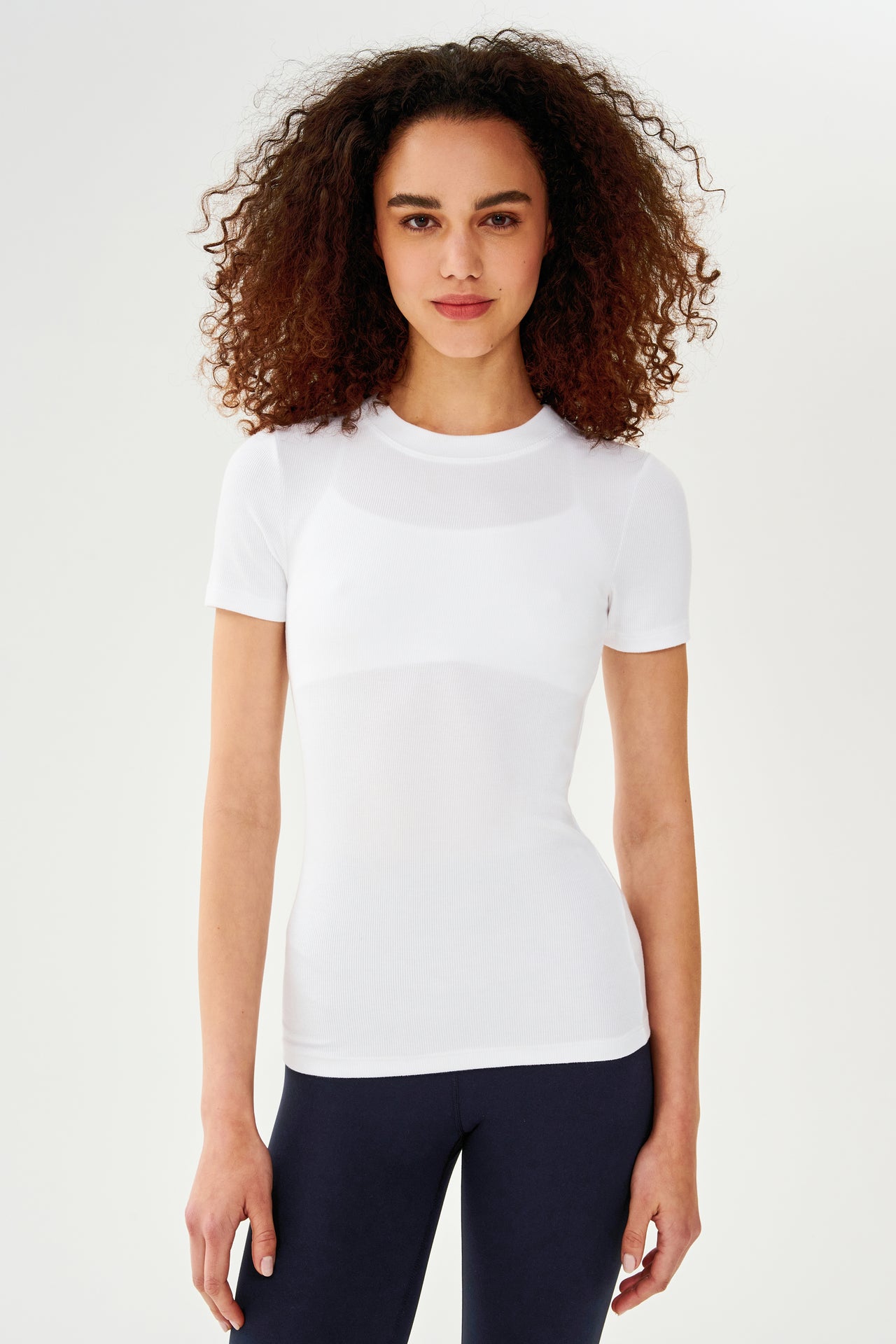 A woman wearing a SPLITS59 Louise Rib Short Sleeve in White and leggings for yoga.