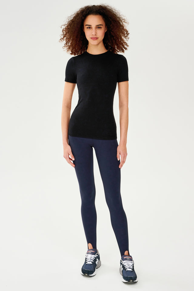 A woman wearing a SPLITS59 Louise Rib Short Sleeve in Black and blue leggings, ready for her yoga session.