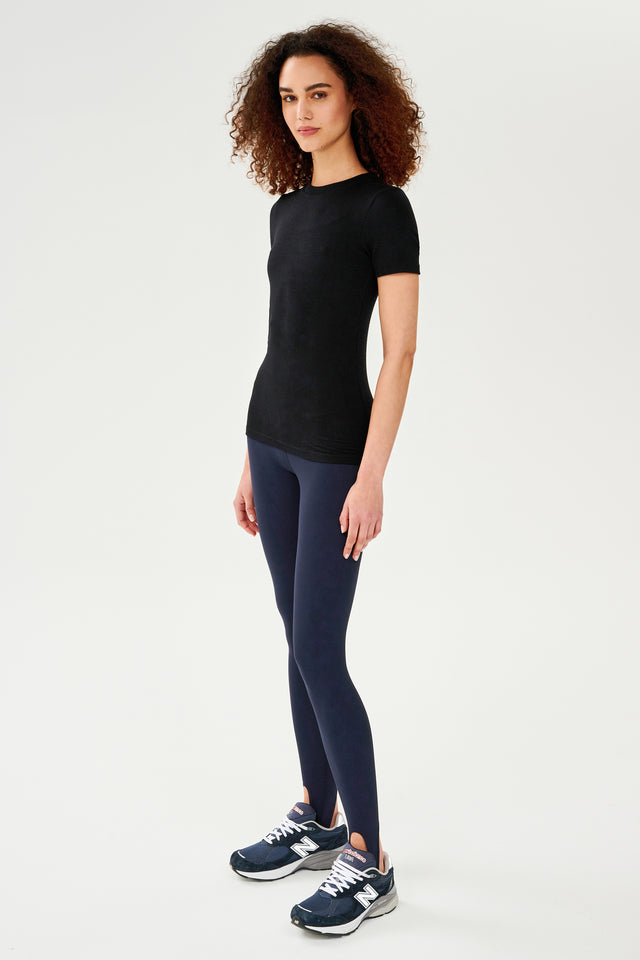 A woman wearing black leggings and a SPLITS59 Louise Rib Short Sleeve - Black, ready for her gym workouts.