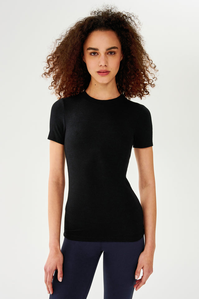 A woman wearing a SPLITS59 Louise Rib Short Sleeve - Black t-shirt and leggings for yoga.