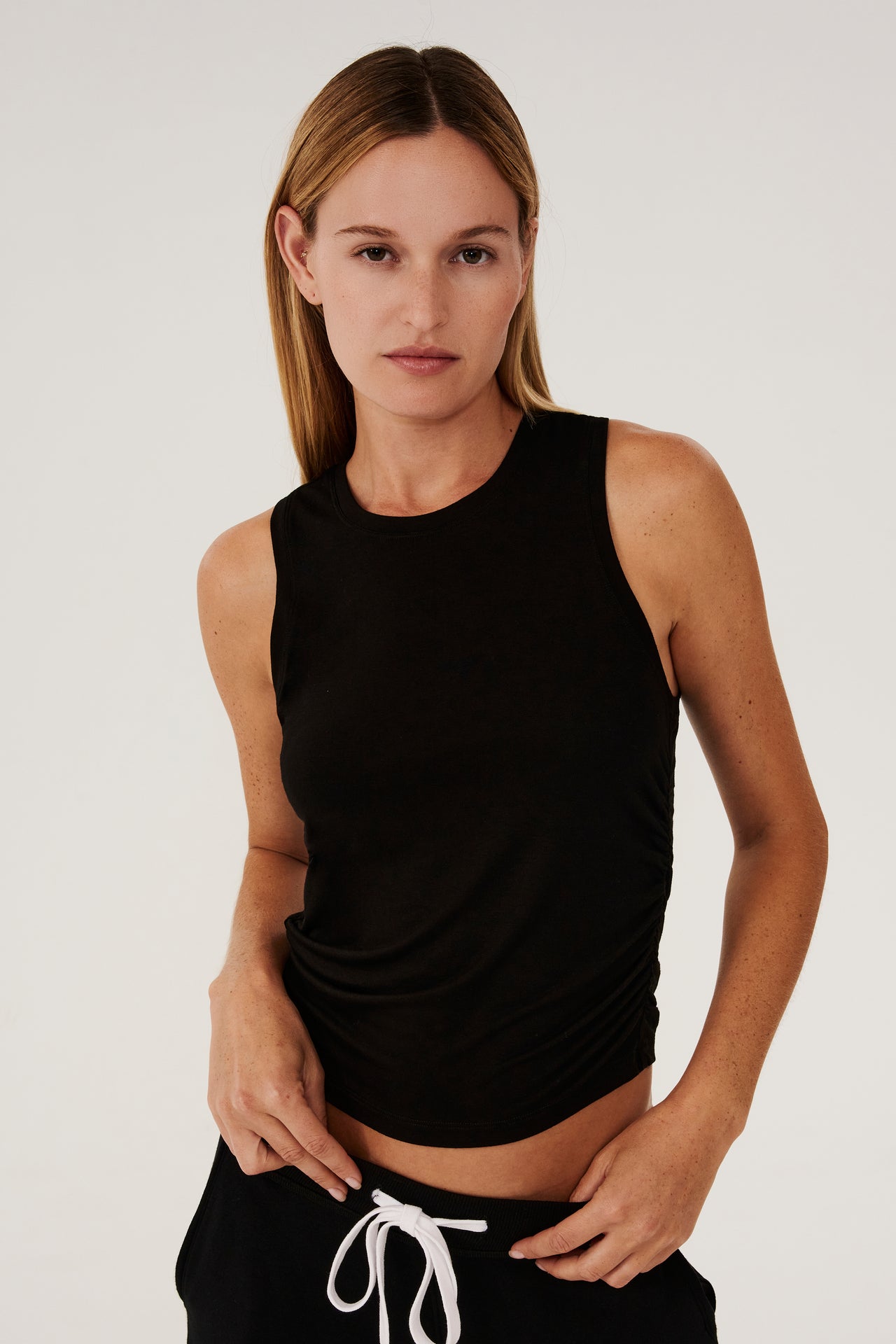 A woman layering a SPLITS59 Frida Jersey Tank - Black for gym workouts and black sweatpants.