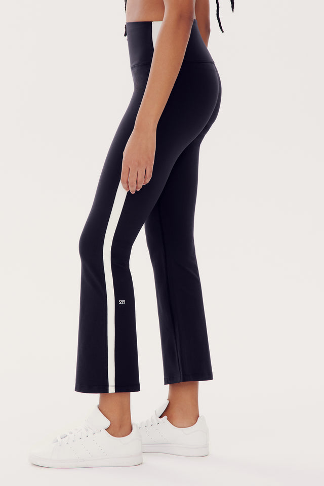 Person wearing SPLITS59 Raquel High Waist Crop - Black/White with a white side stripe made of nylon and spandex, paired with white sneakers against a white background.
