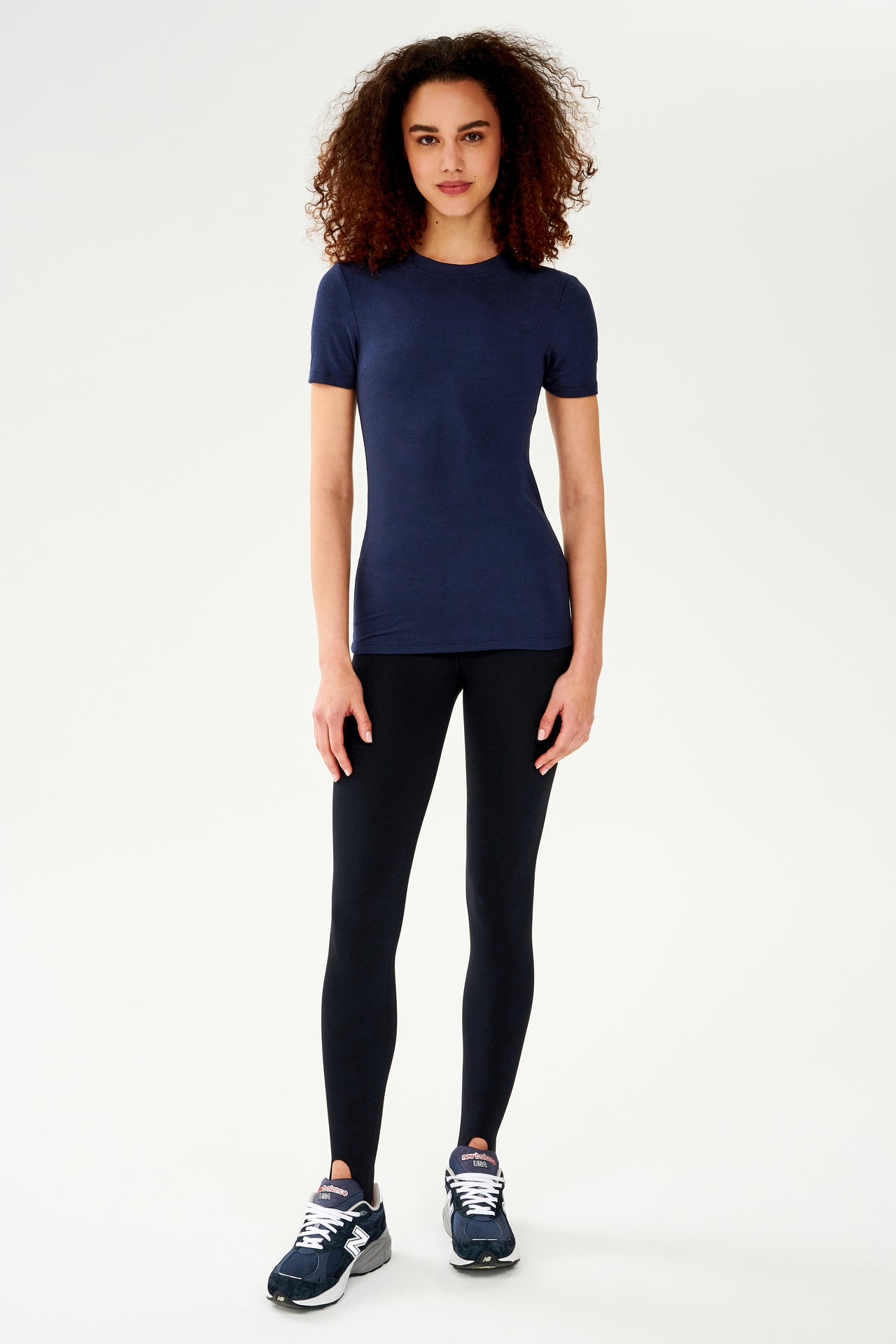 A woman wearing a SPLITS59 Louise Rib Short Sleeve in Indigo and black leggings, ready for her yoga session.