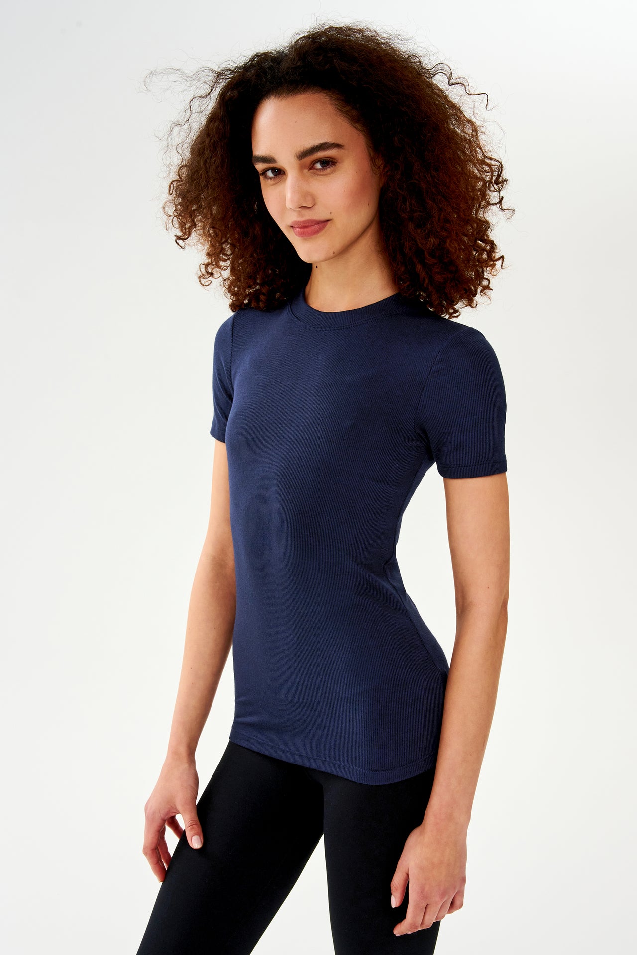 A woman wearing a SPLITS59 Louise Rib Short Sleeve in Indigo and black leggings is ready for her yoga session.