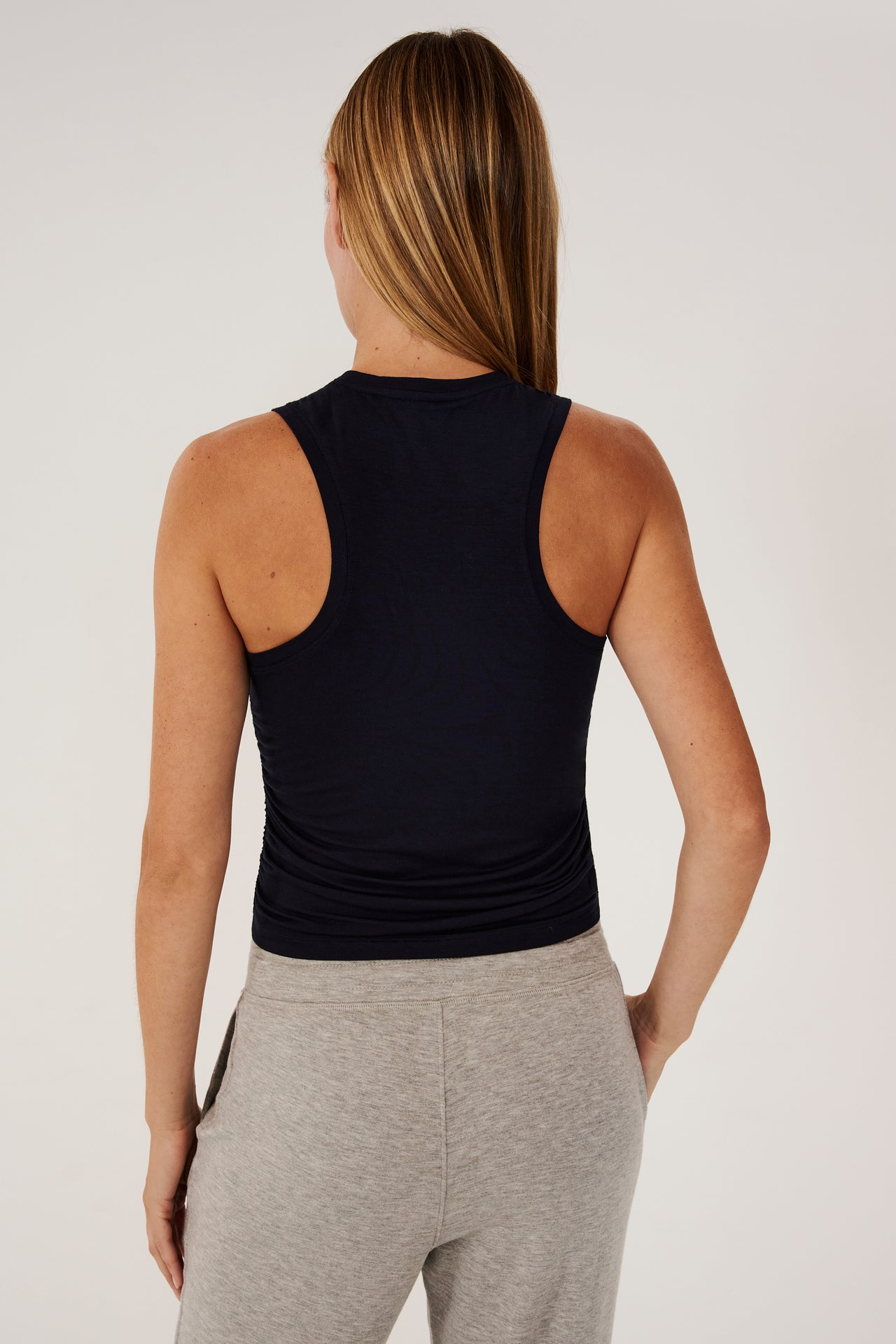 The back view of a woman layering a SPLITS59 Frida Jersey Tank - Indigo over her gym outfit, paired with grey sweatpants.