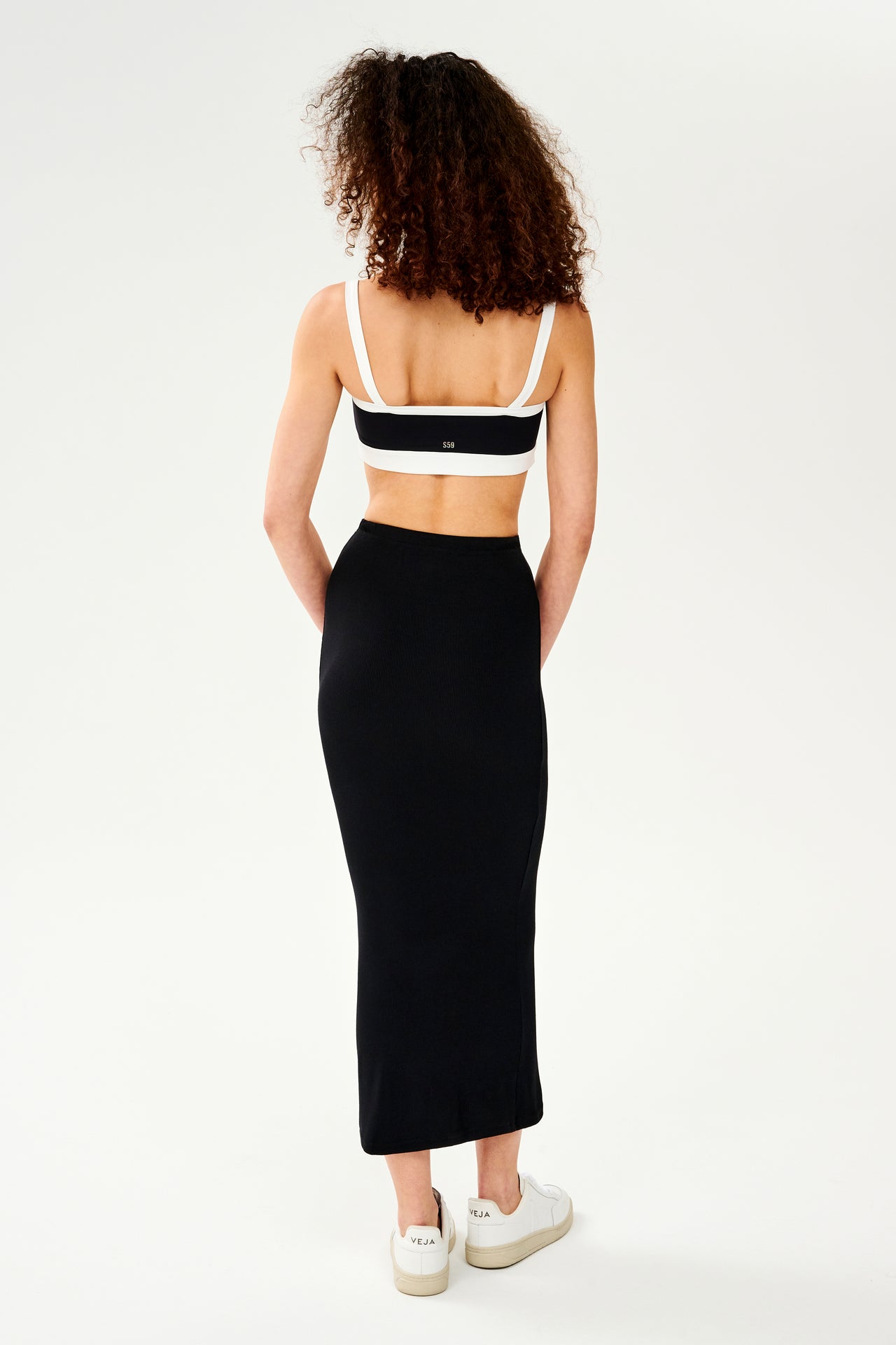 The back view of a woman lounging at home in a black and white SPLITS59 Kiki Rib Maxi Skirt.