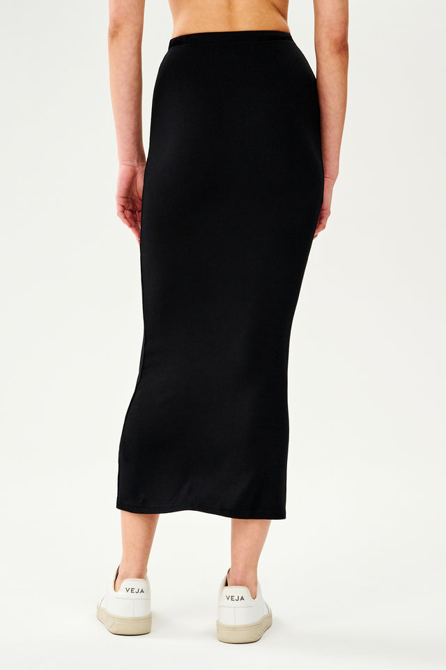 The back view of a woman lounging at home in her SPLITS59 Kiki Rib Maxi Skirt - Black.