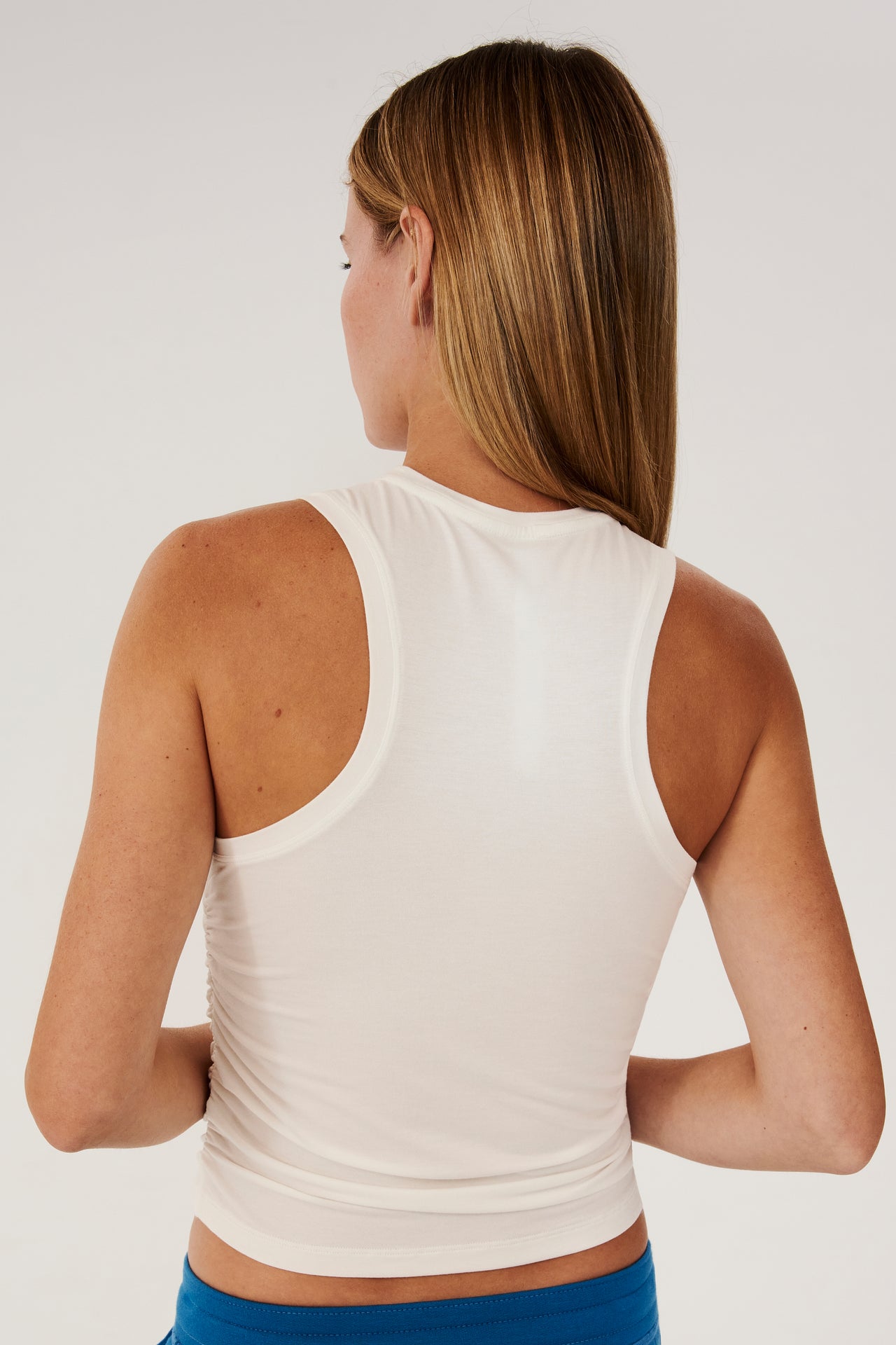 The back view of a woman wearing a SPLITS59 Frida Jersey Tank in White, perfect for gym workouts, and blue pants.