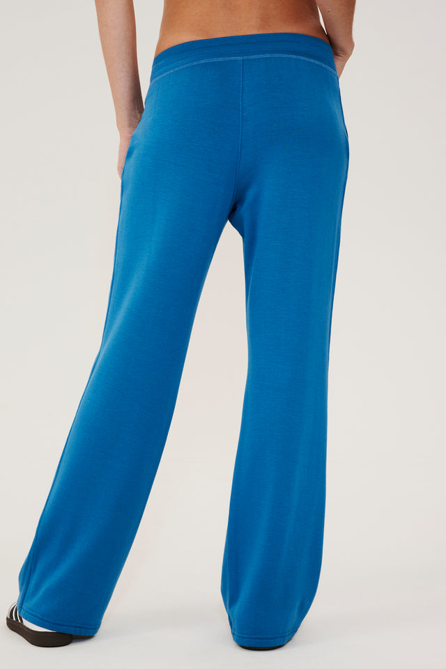 Back view of woman wearing a bright blue high rise wide leg relaxed fit sweatpant with side pockets. Paired with white and grey shoes with black stripes.