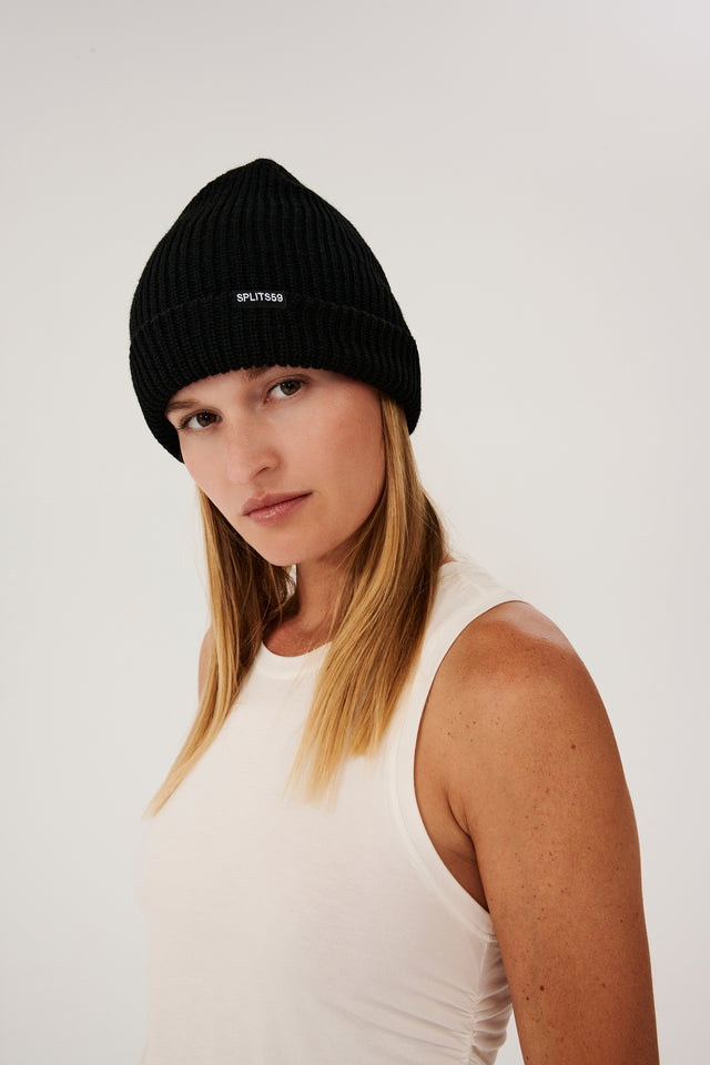 Side view of a girl in a black beanie with splits 59 logo and a white tank top