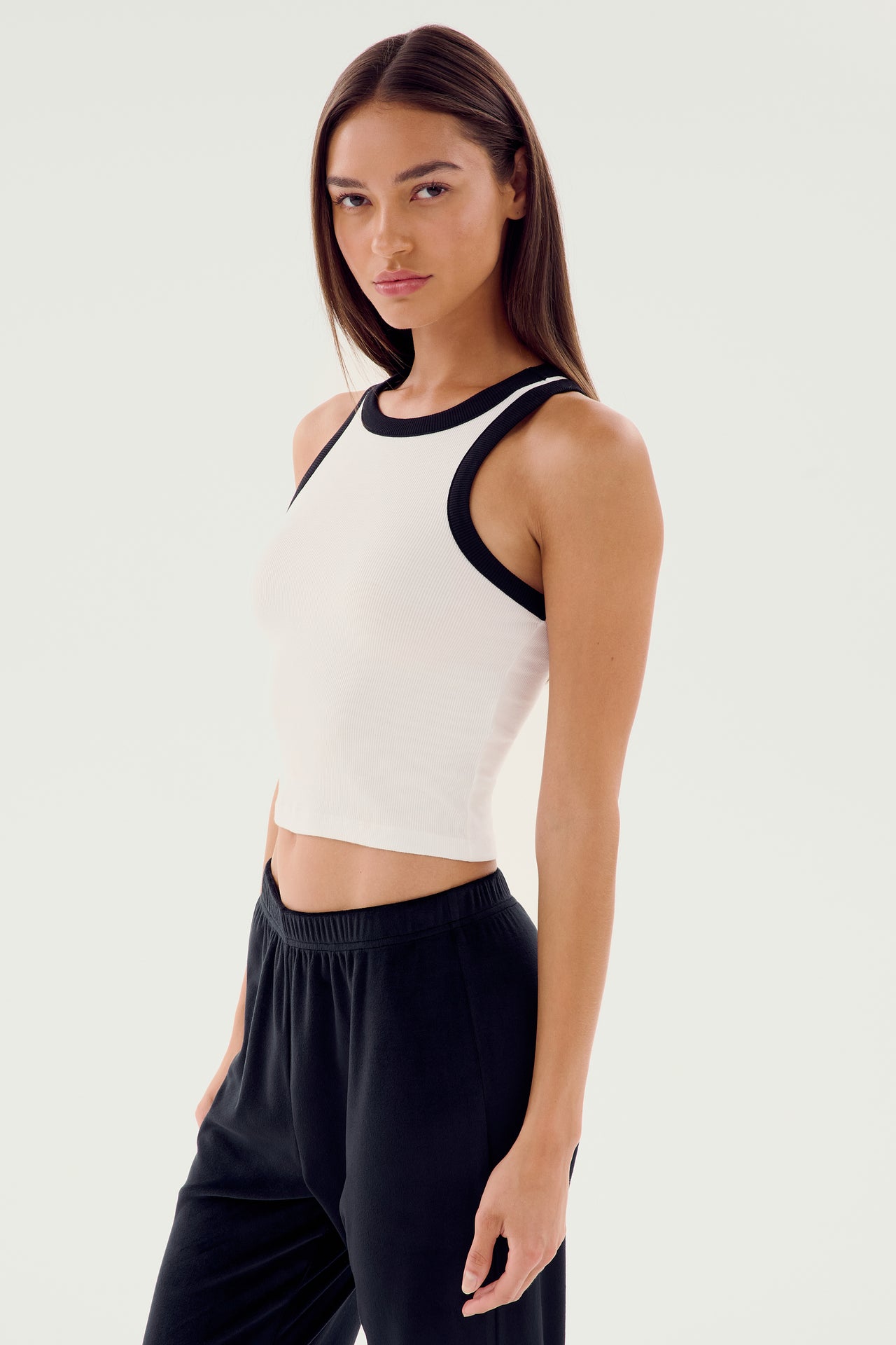 A person with long dark hair wears the Kiki Rib Crop Tank in white and black from SPLITS59, paired with black pants, standing against a plain white background.