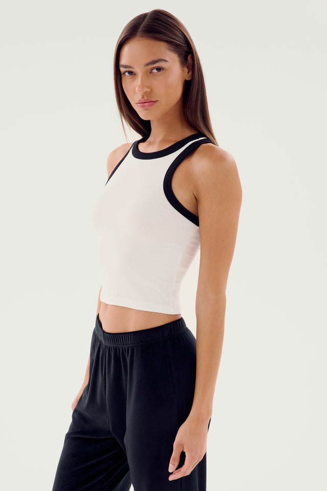 A person with long dark hair wears the Kiki Rib Crop Tank in white and black from SPLITS59, paired with black pants, standing against a plain white background.