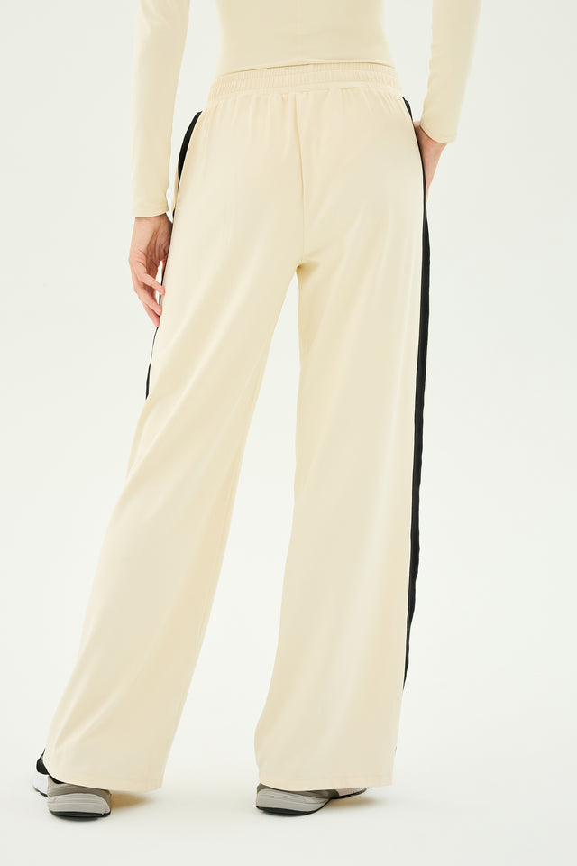 A person is wearing the SPLITS59 Luca Airweight Trouser with Stripe in Creme/Black, highlighting its stylish design as they stand facing away to emphasize the elegance and comfort of the ultra-luxe Airweight fabric.