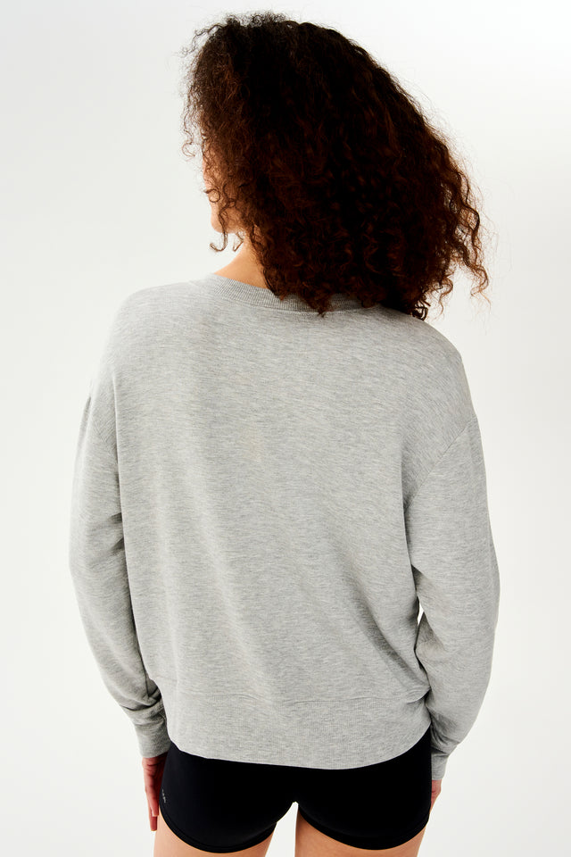Back view of woman with curly dark brown hair wearing a light grey crewneck sweatshirt and black shorts 