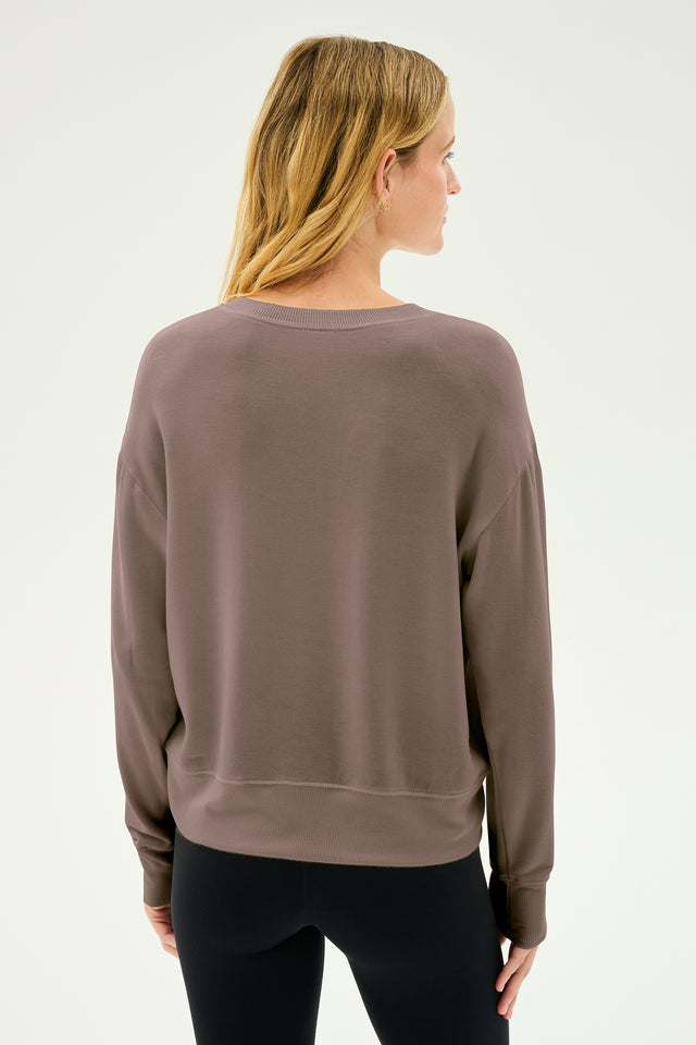 A person stands with their back to the camera, highlighting the Sonja Fleece Sweatshirt in Lentil by SPLITS59, paired with black pants, all set against a neutral background.