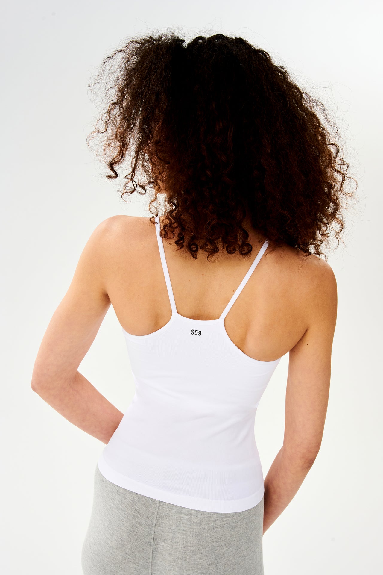 The back of a woman wearing a SPLITS59 Loren Seamless Waist Length Tank in White with a shelf bra.