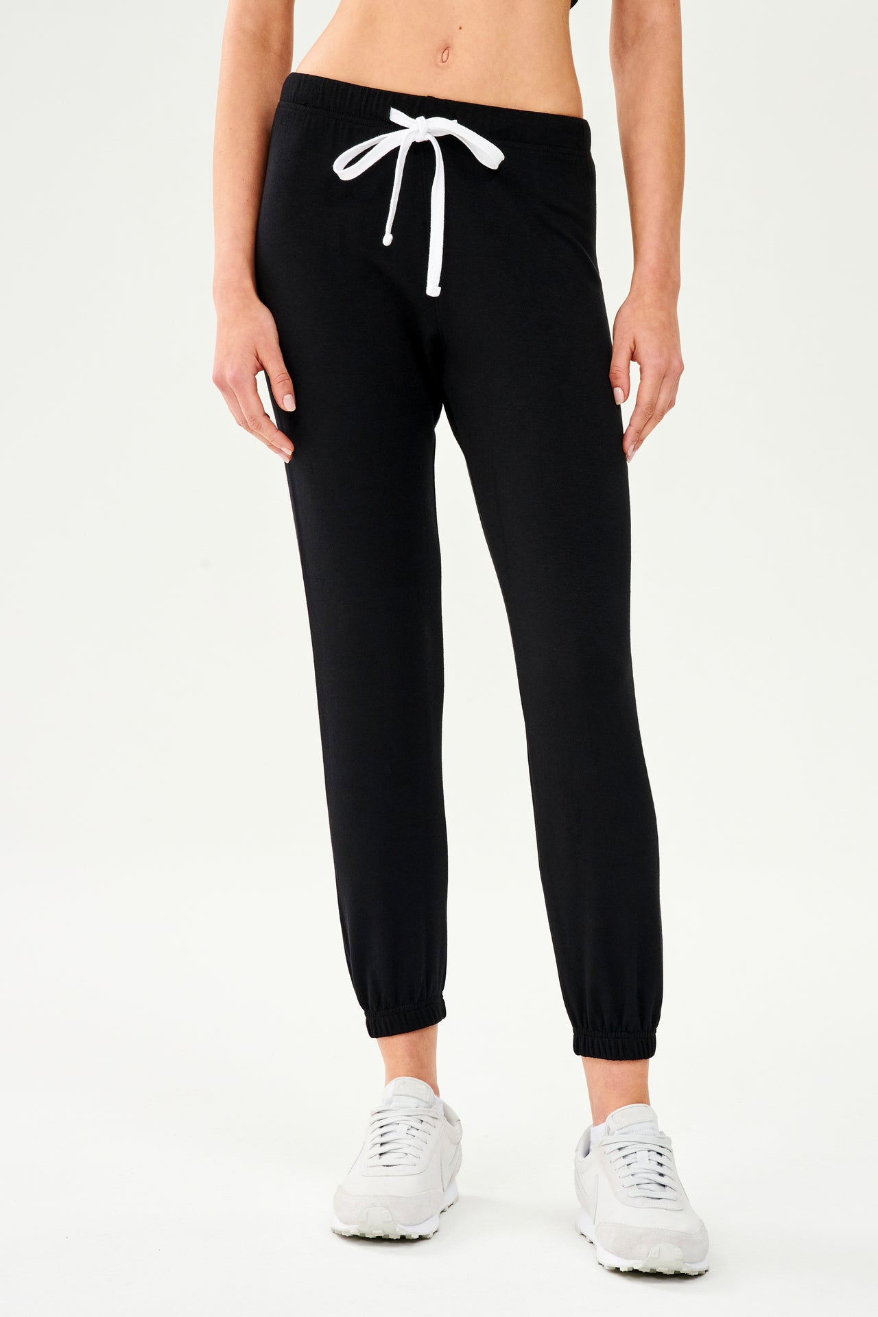 Front view of woman wearing black jogger sweatpant with white drawstring paired with white shoes