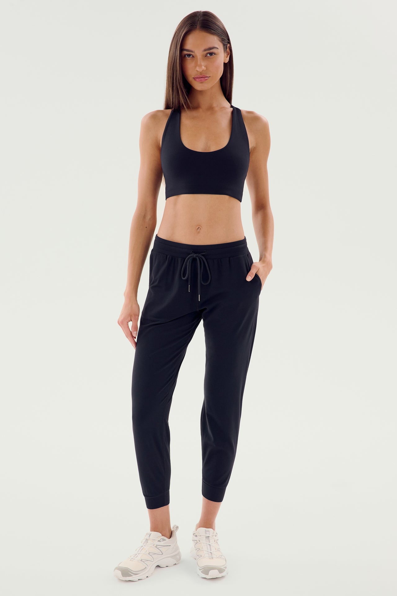 A person wearing a black sports bra, the Classic Airweight Jogger in black from SPLITS59, and white sneakers poses against a plain white background.