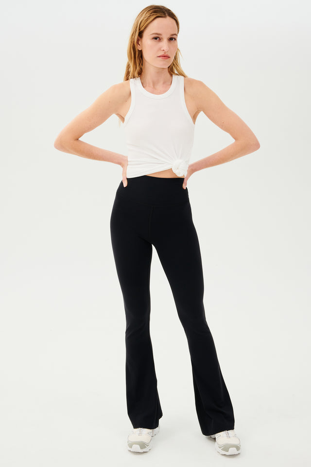 A woman wearing Raquel High Waist Airweight Flare leggings in black made by SPLITS59 and a white tank top.