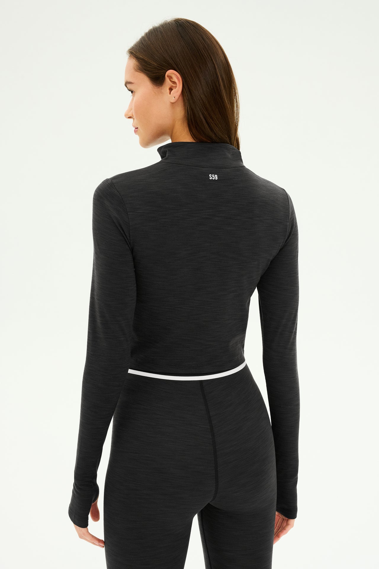 An individual wearing the SPLITS59 Stevie Active Rib Half Zip in Heather Graphite faces away. This black, long-sleeve athletic top, crafted from active rib fabric, displays a small logo on the back, ideal for gym workouts.