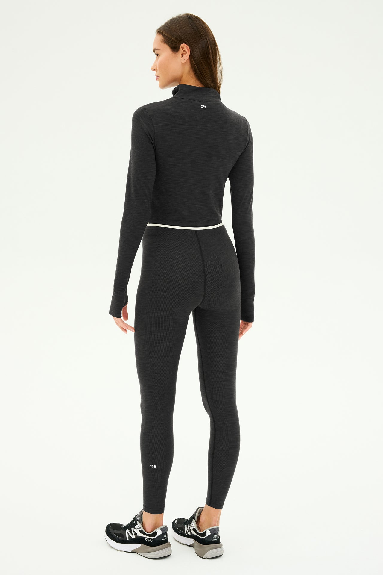 A person wearing the Stevie Active Rib Half Zip in Heather Graphite by SPLITS59 pairs it with leggings and sneakers, facing away in a neutral pose against a plain background.