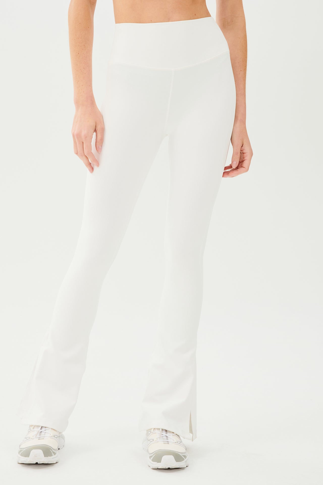 A woman wearing SPLITS59 Raquel High Waist Flare w/ Split Hem leggings in white workout fabric and a white top.