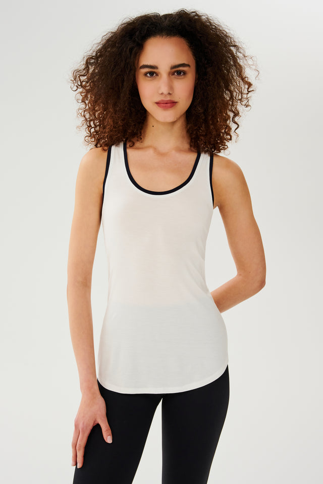 A woman wearing a SPLITS59 Hana Ringer Tank - White/Indigo and black leggings, perfect for gym workouts.