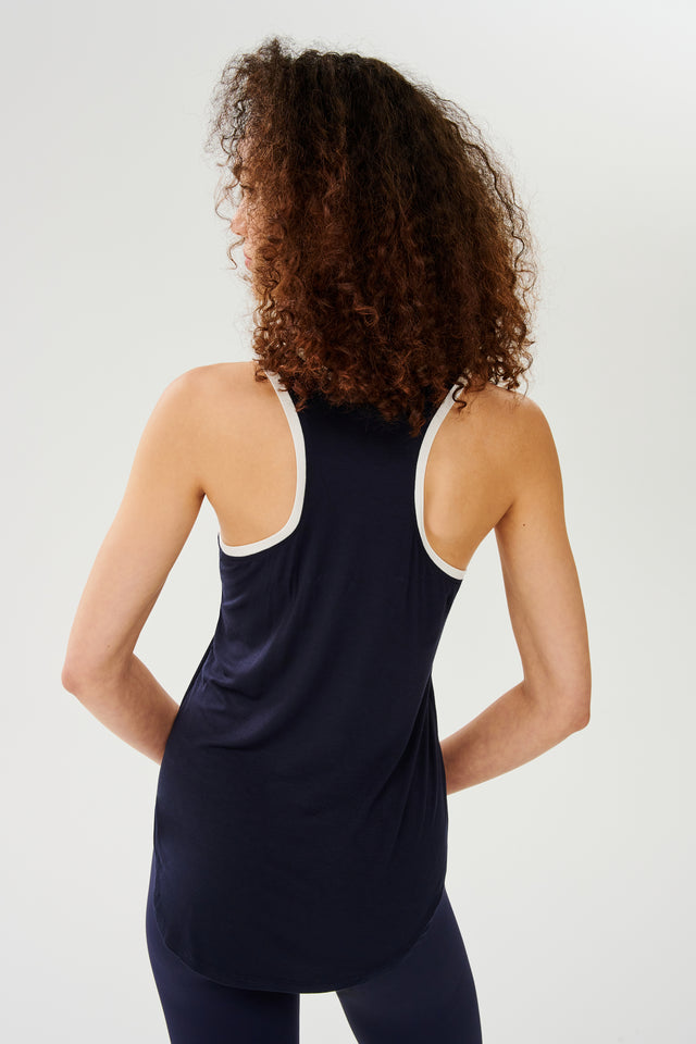 The back view of a woman wearing a SPLITS59 Hana Ringer Tank - Indigo/White and leggings, perfect for layering or a workout.