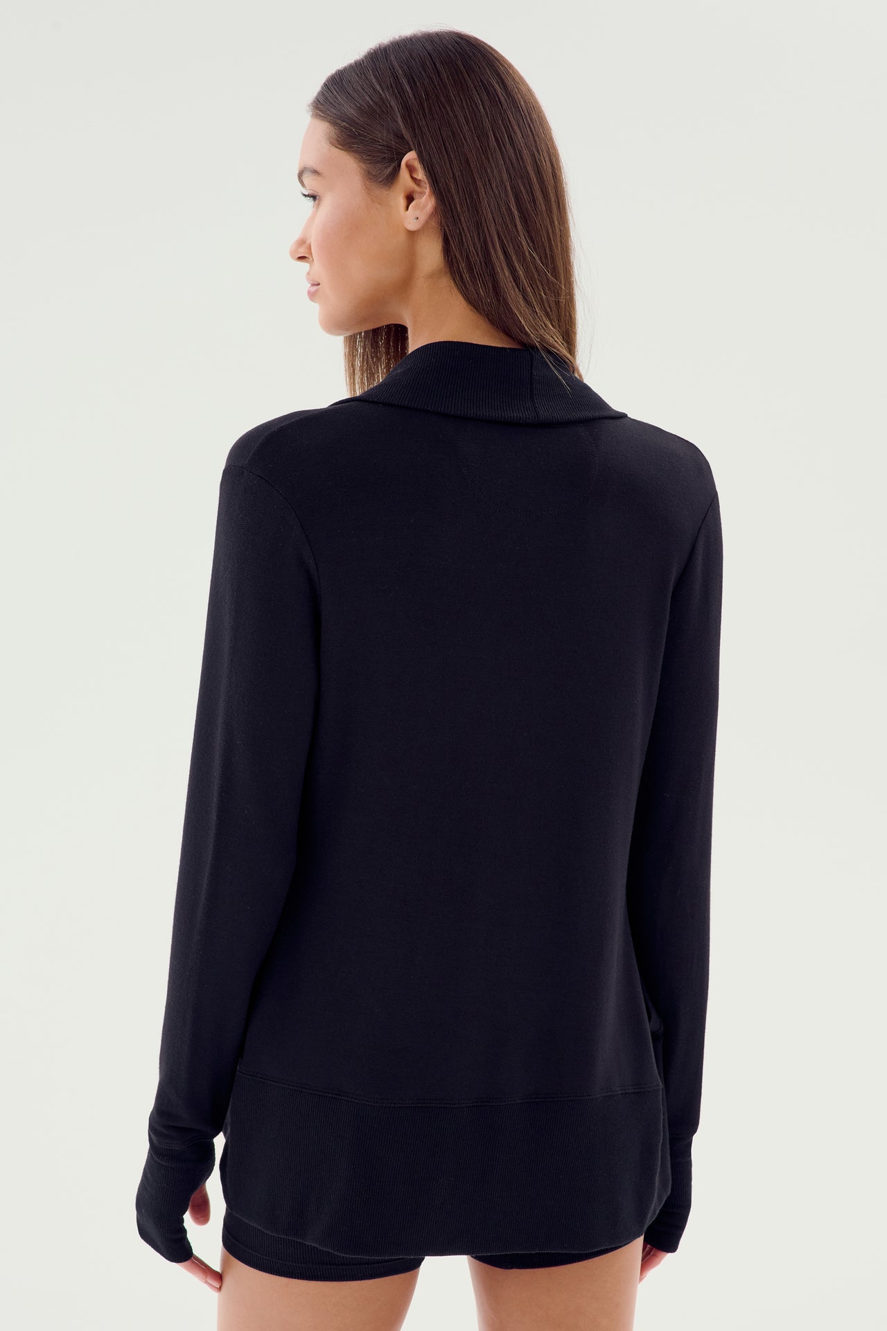 A person with long, straight hair, wearing a Celine Fleece Cardigan in black by SPLITS59 from their active wardrobe staple, is standing and facing away from the camera against a light background in Los Angeles.