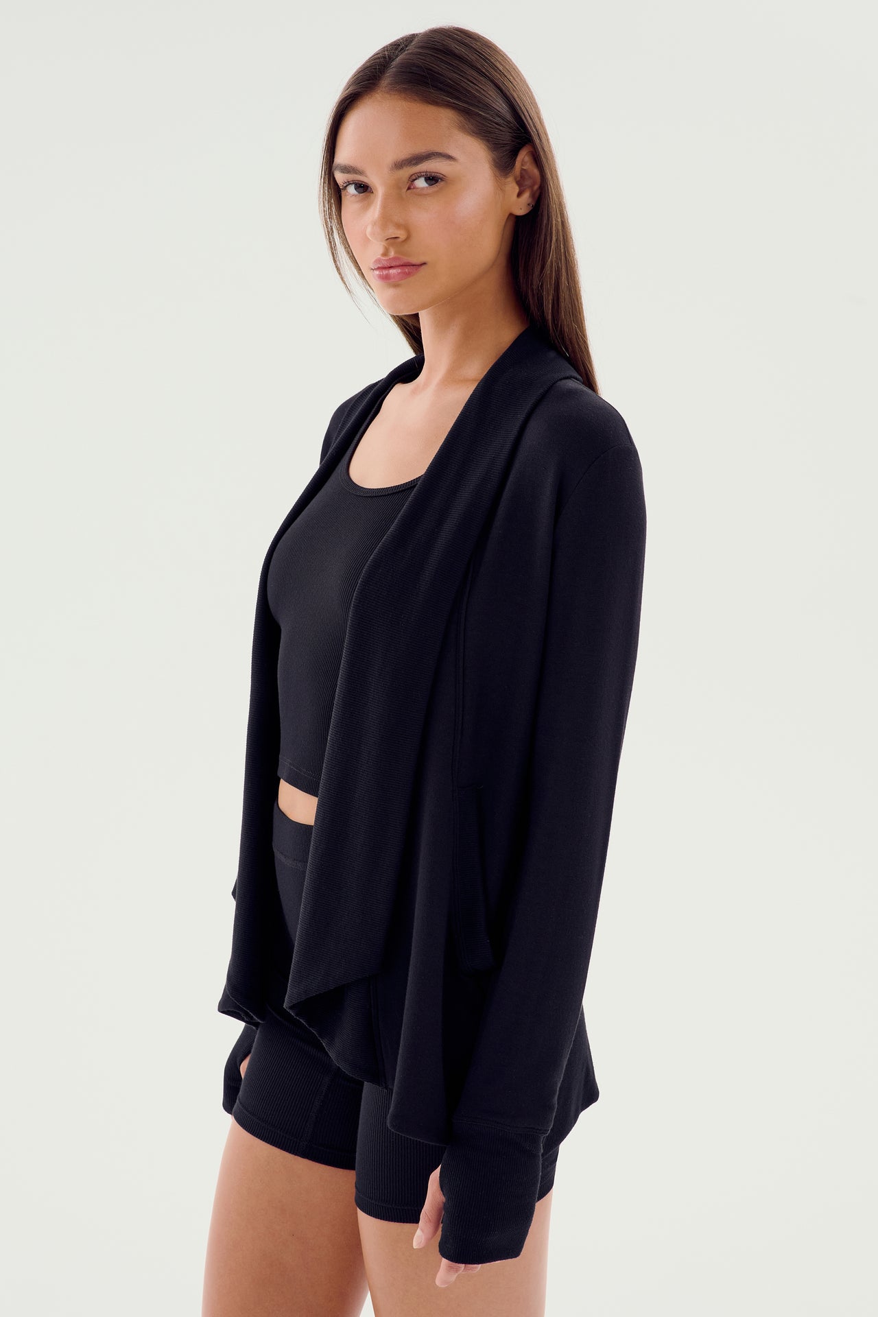 A person is wearing the Celine Fleece Cardigan in black by SPLITS59 over a black top and black shorts, standing against a plain white background.