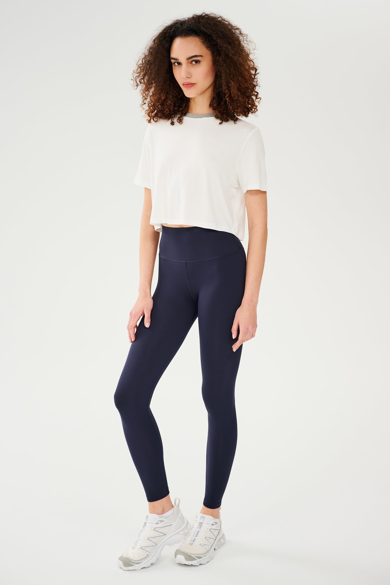 Full side view of girl wearing white cropped short sleeve t-shirt with thin light grey neck hem and dark blue leggings with white shoes