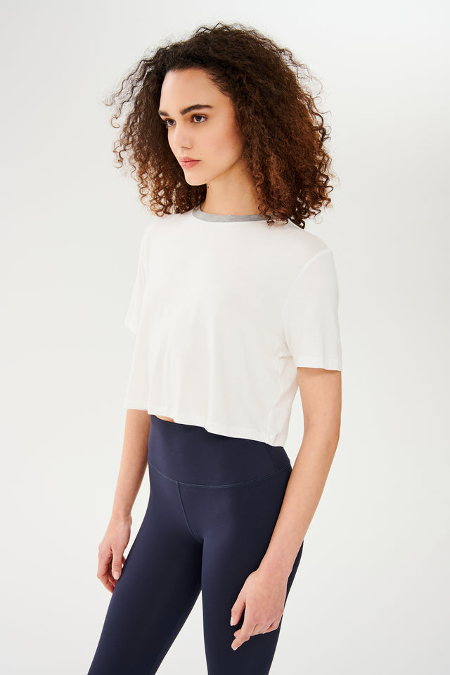 Side view of girl wearing white cropped short sleeve t-shirt with thin light grey neck hem and dark blue leggings 