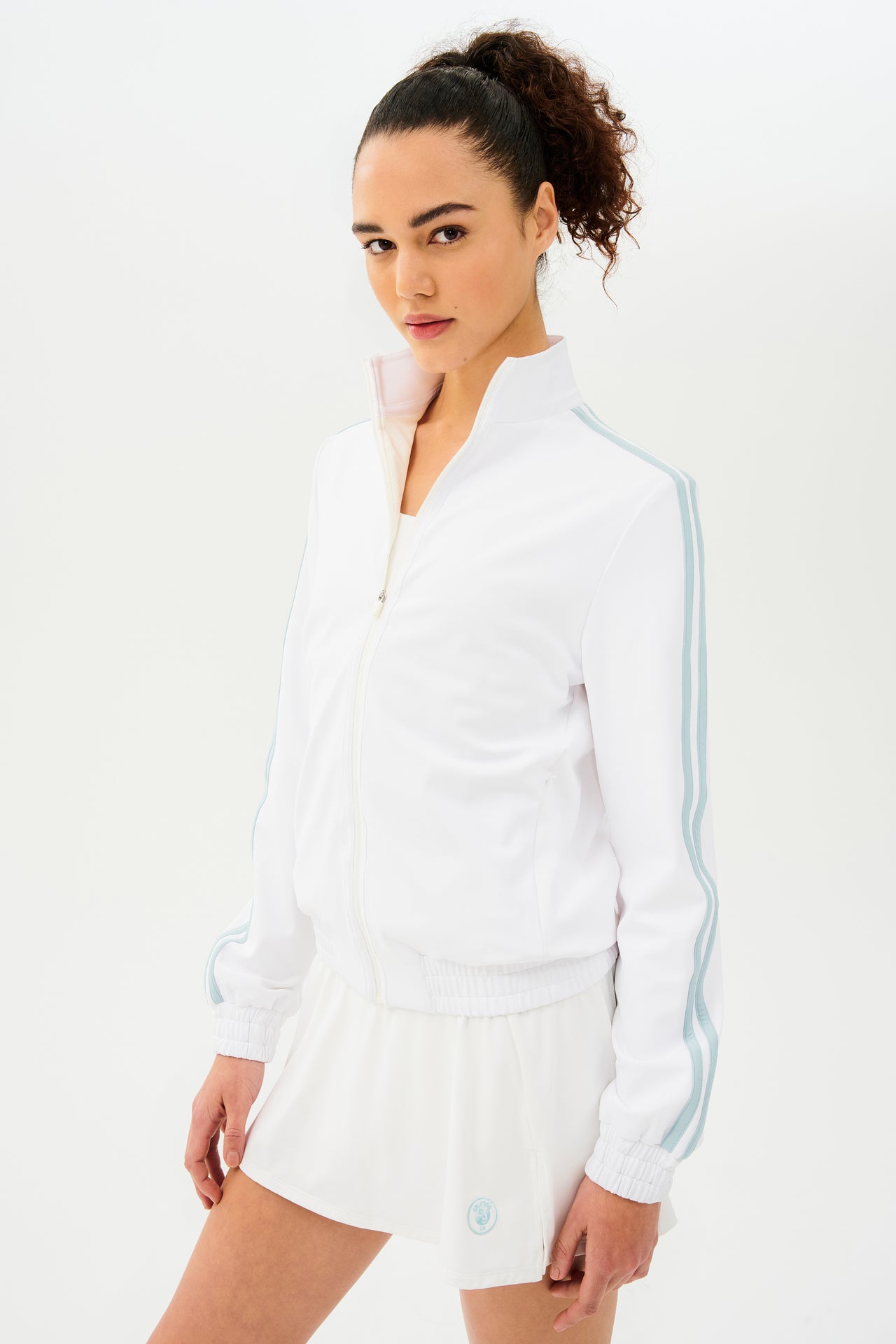 A woman wearing a SPLITS59 Fox Techflex Jacket in White/Teal for a retro vibe workout outfit.