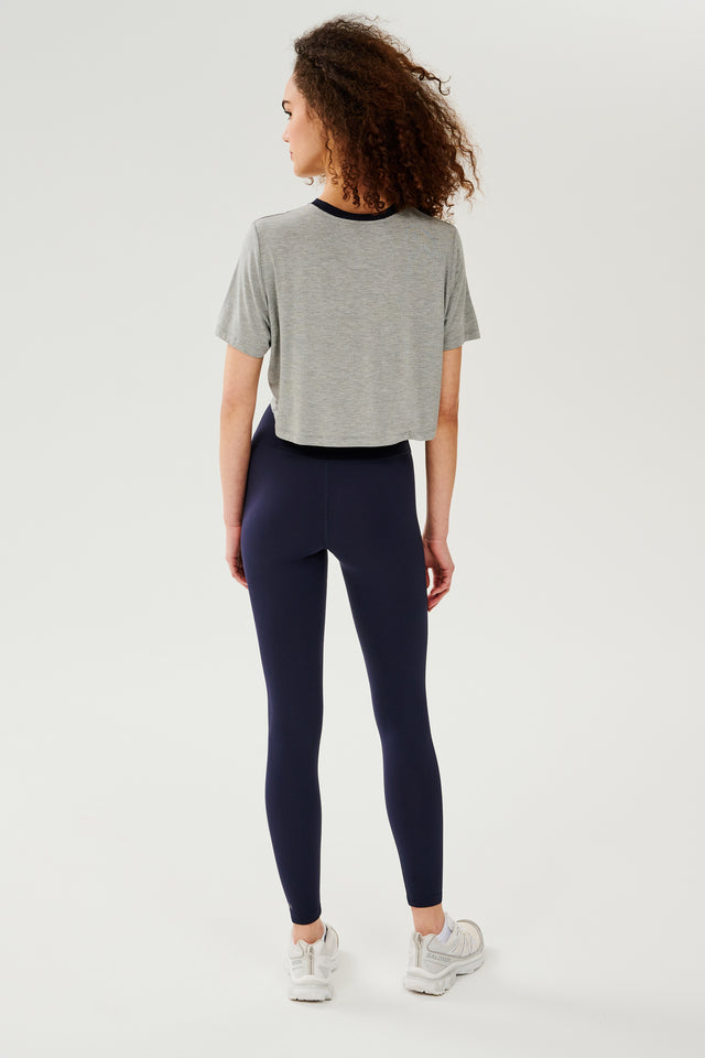 Full back view of girl wearing  light grey cropped short sleeve t-shirt with thin dark blue neck hem and dark blue leggings with white shoes